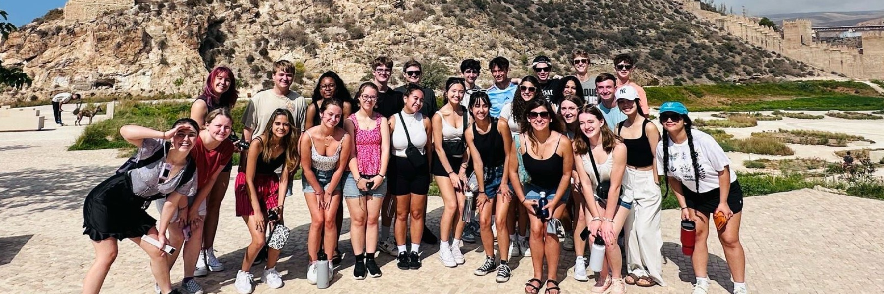 A group of students stands in front of a desert landscape with a ruins in the back