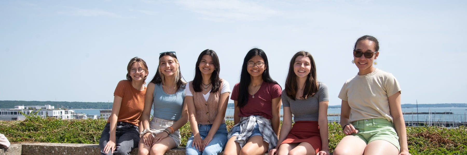 Six students sit on a wall in France on a bright day
