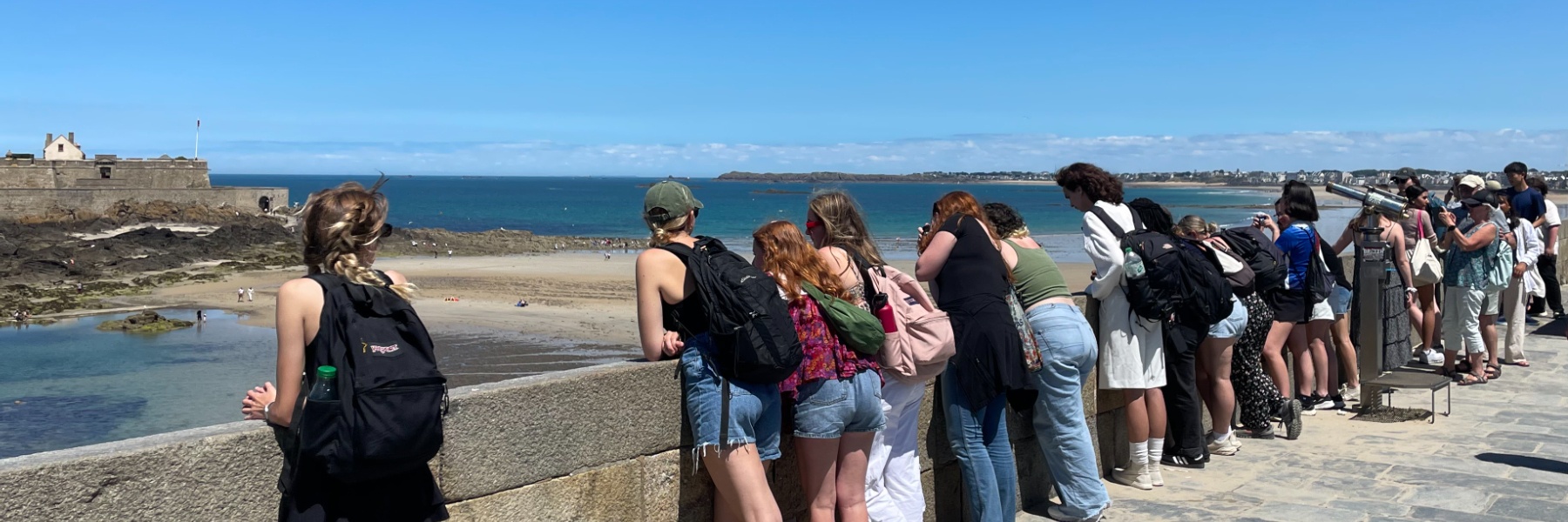 Students look off a castle rampart into a body of water on a clear day