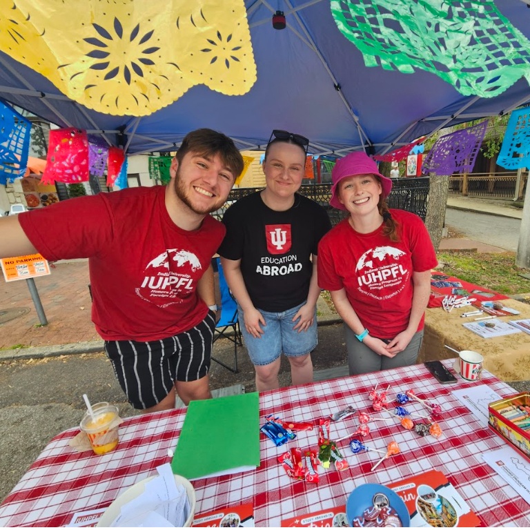 Three workers pose under a tent behind a table with candy and promotional materials
