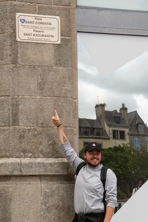 Young man in a baseball cap points up towards a sign on a stone structure