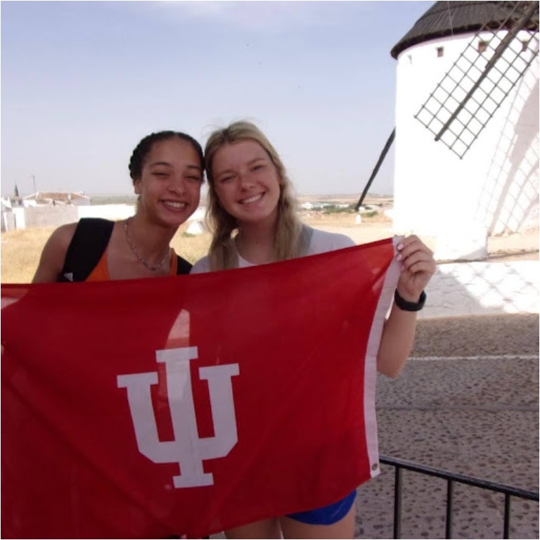 Two IUHPFL students pose with the IU flag in front of some windmills