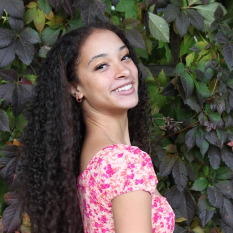 A young woman in a pink top looks over her shoulder at the camera