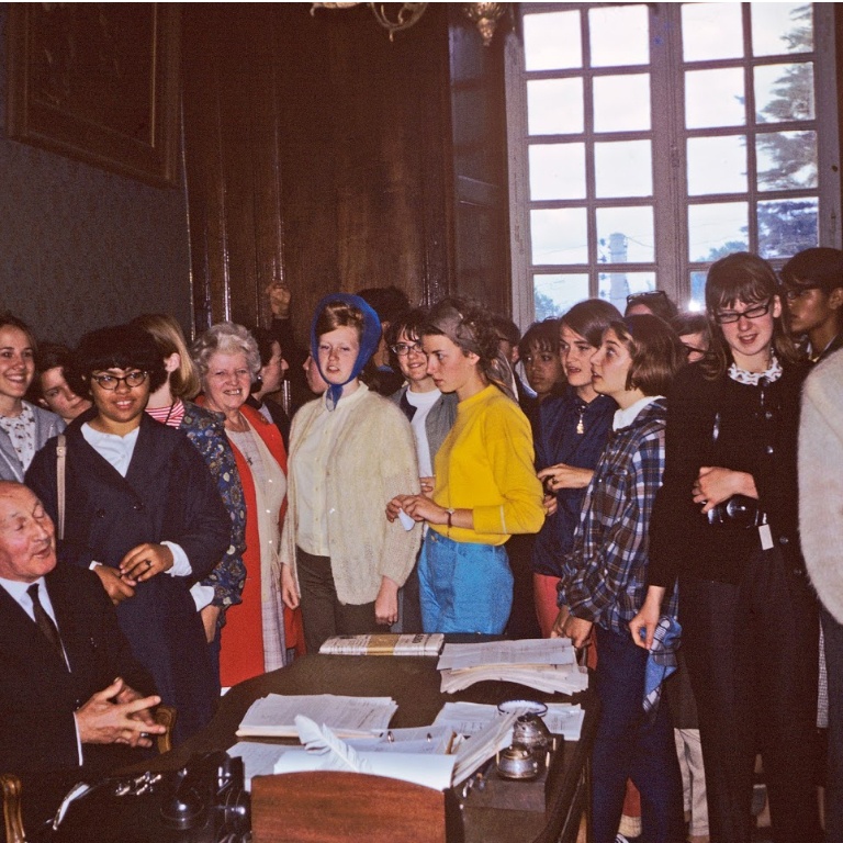 The students of the 1966 Saint-Brieuc group stand around the mayor who is seated at his desk