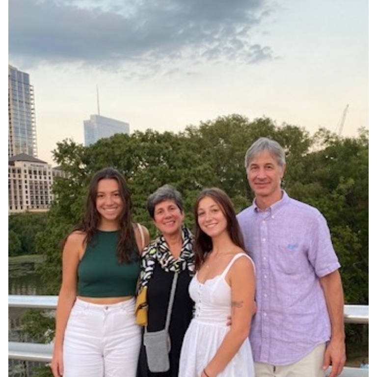 A family with two daughters and two parents pose in front of a body of water