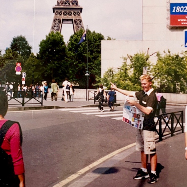 A young man holding a map points at the Eiffel Tower in the background