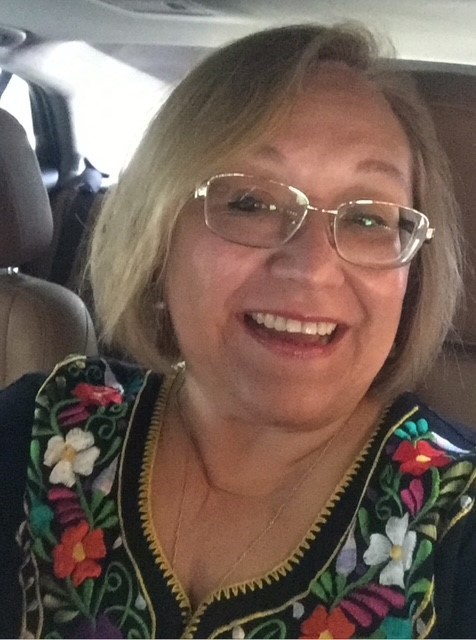 A woman in a black shirt with floral embroidery poses in her car