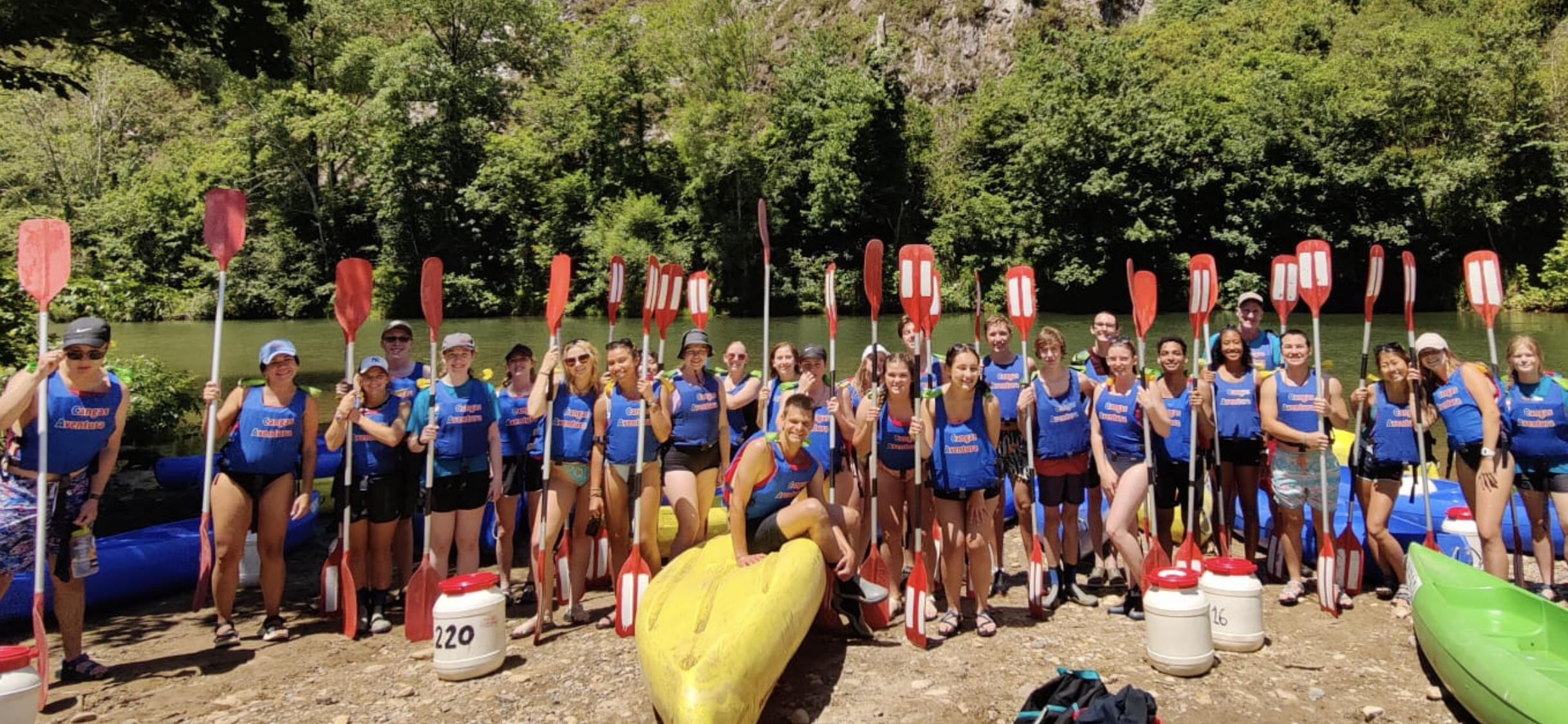 A group of students poses while holding paddles before kayaking