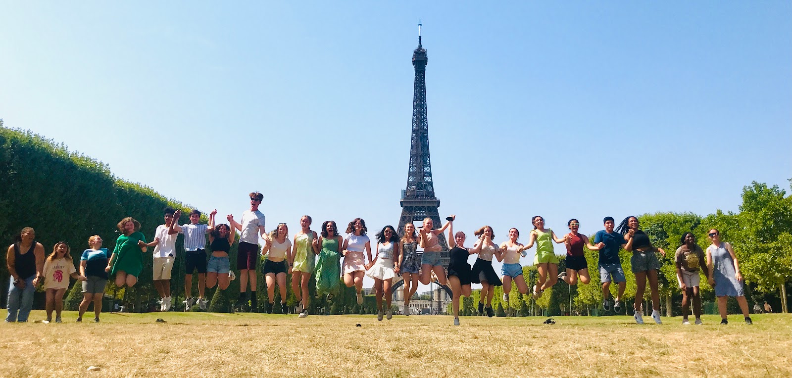 Students hold hands and jump with the Eiffel Tower in the background