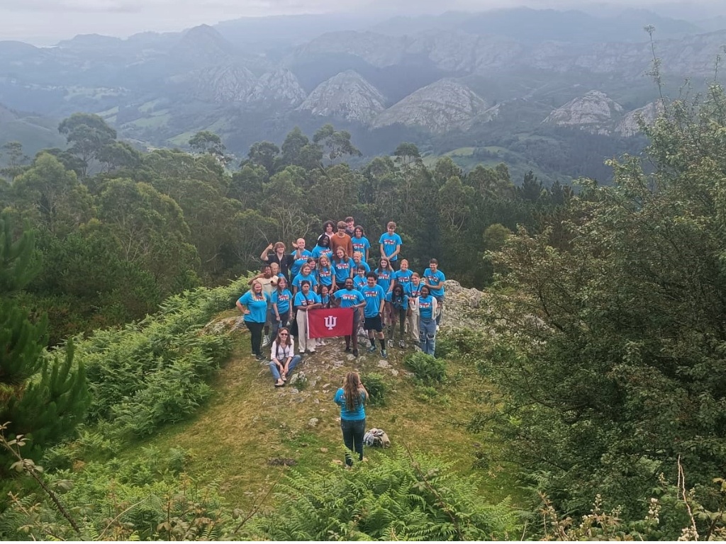 The camera looks down on a group of students in matching turquoise shirts with the mountains in the background