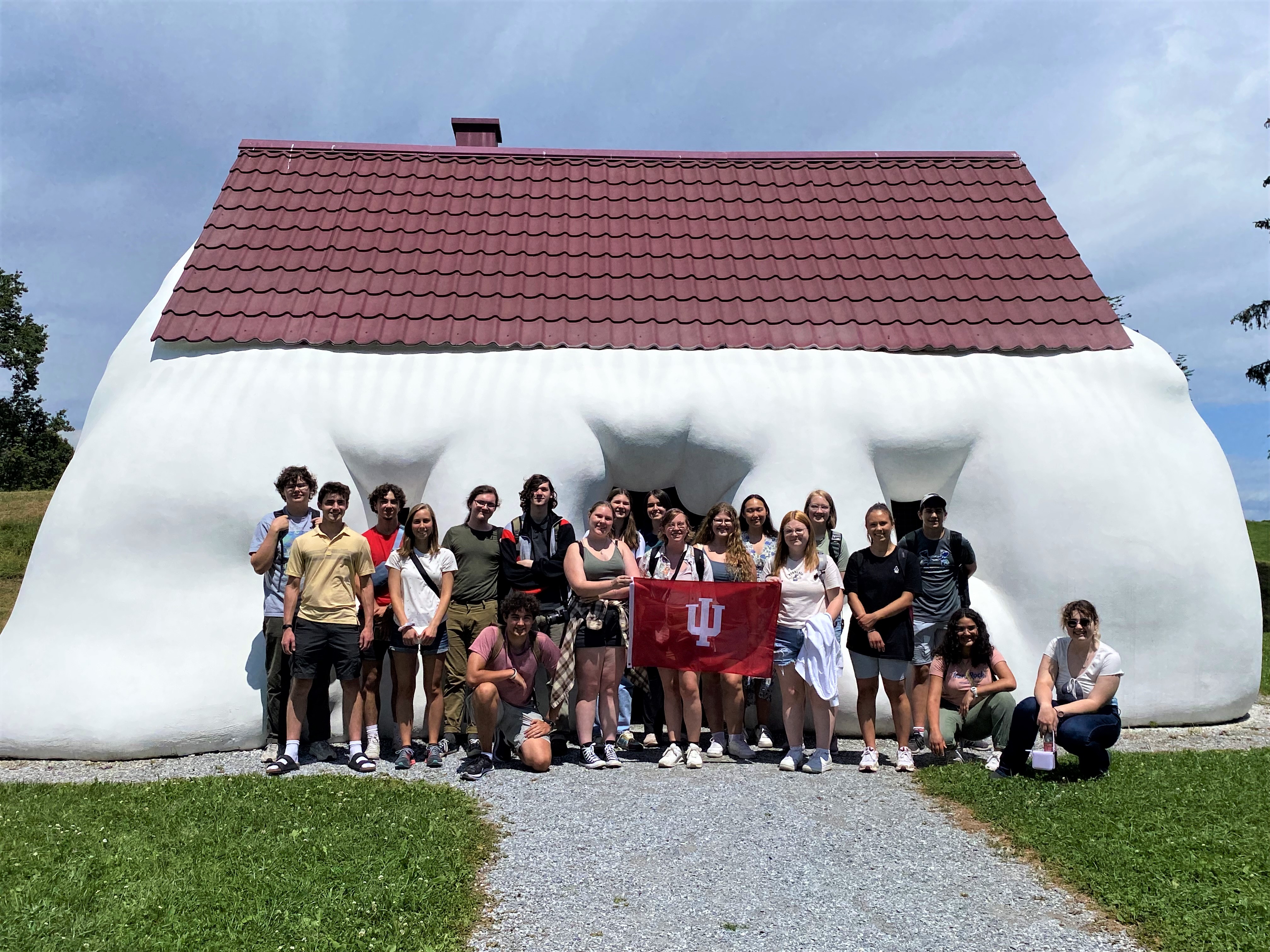 The 2023 Graz team stands in front of a white sculpture with the IU flag